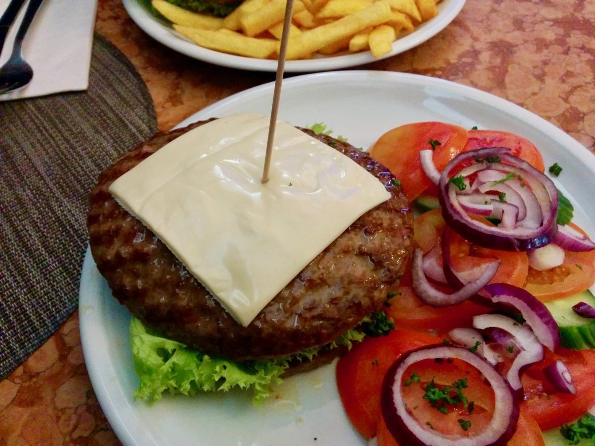 Foto von zwei aufeinanderliegenden runden Hackfleischdingers mit Tomaten und Zwiebeln