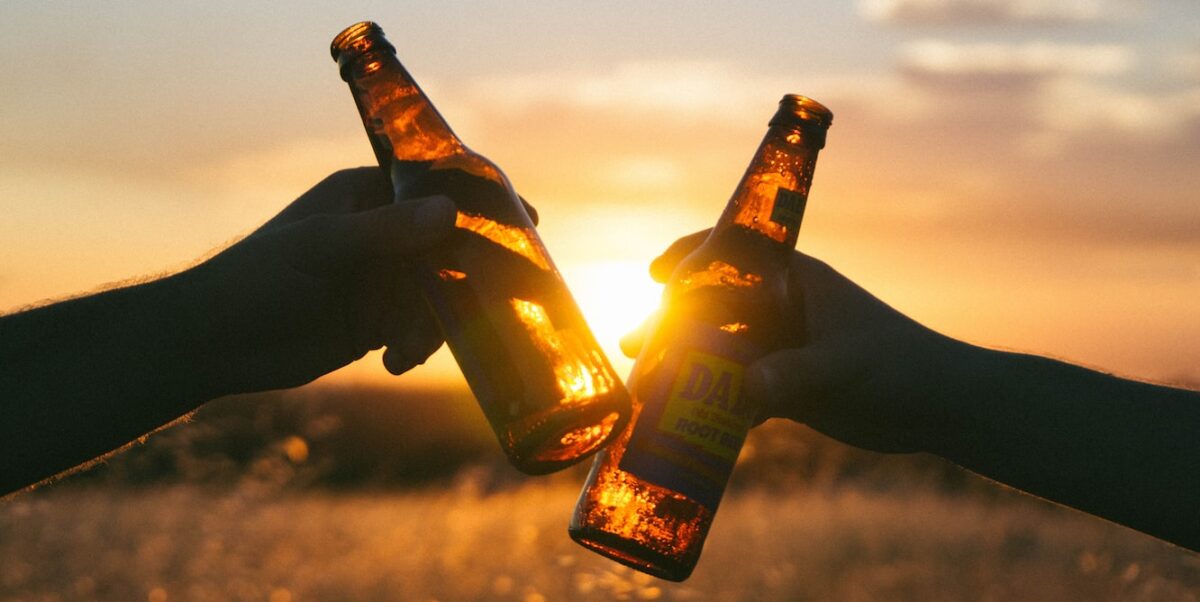 photography of person holding glass bottles during sunset